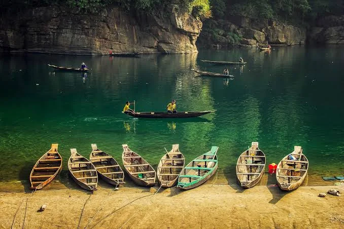 Boats on a clear river between forested cliffs in Meghalaya